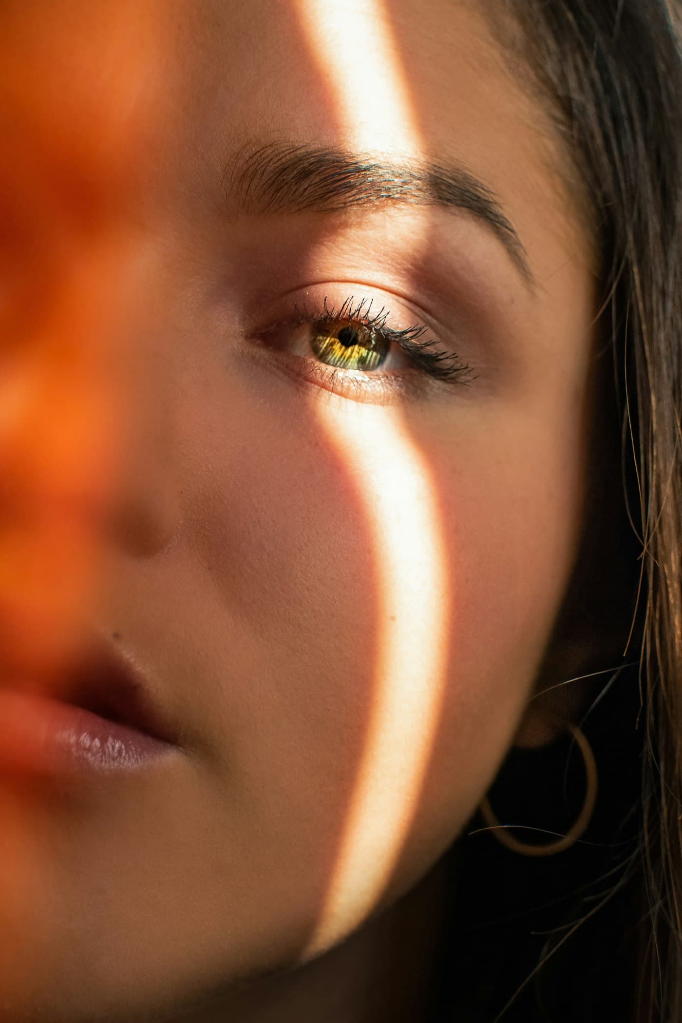 Meio-rosto iluminado por um feixe de luz quente, símbolo do olhar atento da dermatologia